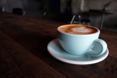 Kapuçino ya da köpüklü latte, ahşap kahve dükkanının arka planında mavi kahve bardağı.