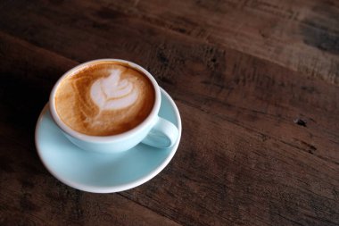 Kapuçino ya da köpüklü latte, ahşap kahve dükkanının arka planında mavi kahve bardağı.