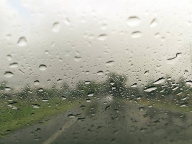 Yağmur mevsimi soyut arka planında yolu olan araba camlarına yağmur damlaları, camlara su damlaları, gece fırtınası araba sürme konsepti