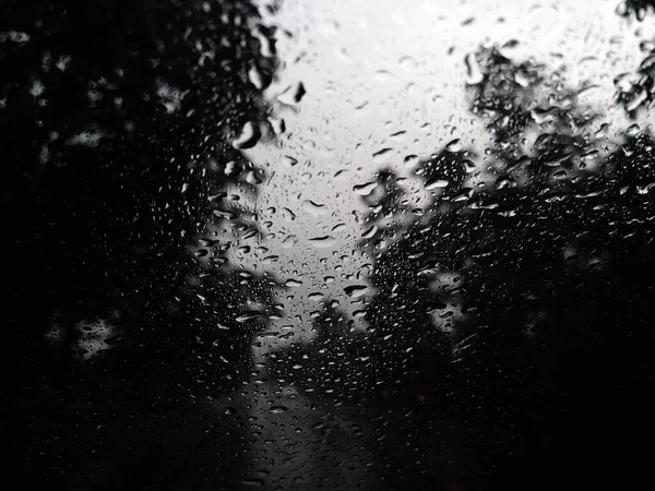 Rain drops on the car glass window with road in rainy season abstract background, water drop on the glass, night storm raining car driving concept