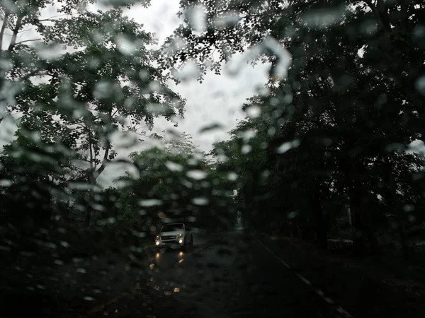 Rain drops on the car glass window with road in rainy season abstract background, water drop on the glass, night storm raining car driving concept