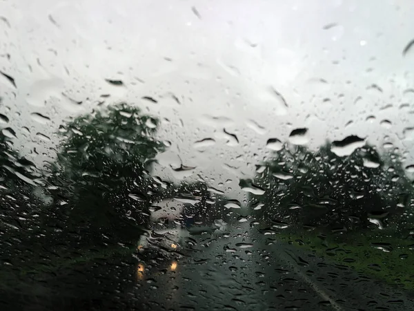 Rain drops on the car glass window with road in rainy season abstract background, water drop on the glass, night storm raining car driving concept