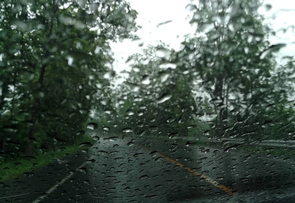 Rain drops on the car glass window with road in rainy season abstract background, water drop on the glass, night storm raining car driving concept