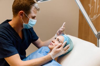 Kadın alın bölgesinde botoks yaptırıyor. Doktor kırışıklıklardan kızın yüzünü temizler. Özel sağlık kliniğinde estetik cerrahi.