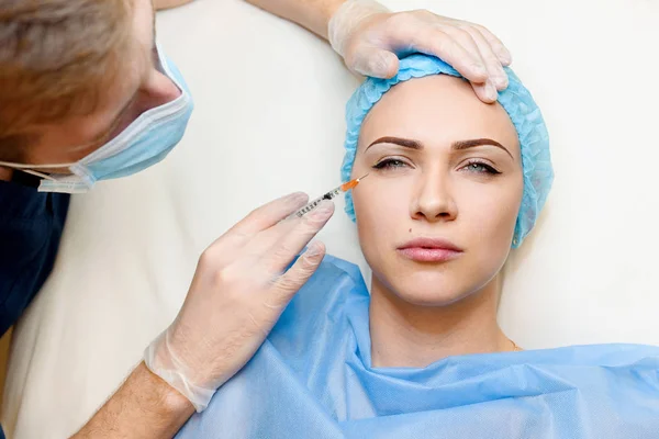 Vrouw maakt botox injecties in de ooghoek. Dokter reinigt het gezicht van het meisje van rimpels. Maak kraaienpootjes vrij door botox injecties. Plastische chirurgie in privé-kliniek. — Stockfoto