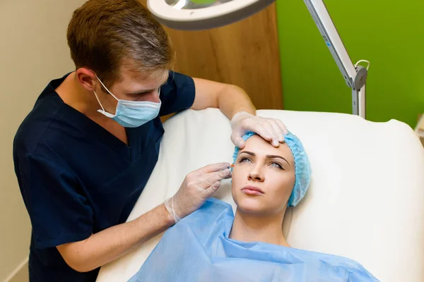 Женщина делает инъекции ботокса в угол глаз. Доктор очищает лицо девушки от морщин. Прозрачные вороньи лапки с помощью инъекций ботокса. Пластическая хирургия в частной клинике . — стоковое фото