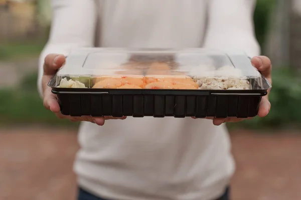 自助寿司在盒装健康食品网上递送服务 穿着白衣的男人送给你一套寿司 日本菜 面包卷 为外卖餐厅做广告 — 图库照片