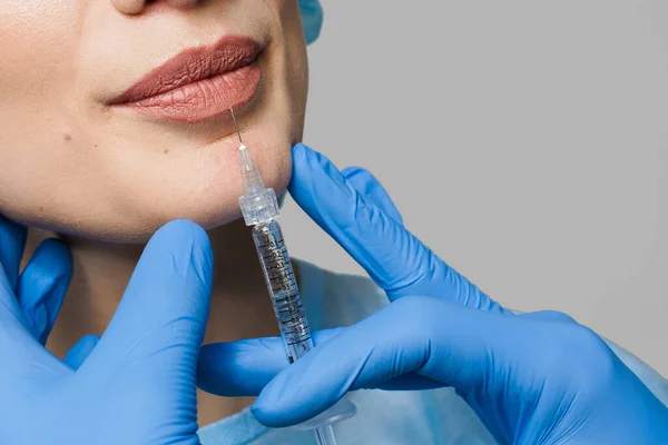 Beyaz arka planda çekici bir kız için yakın dudak büyütme iğneleri. Estetik cerrah tıbbi klinikte dudağına iğne yapar. Kozmetik yenileme yüz tedavisi. Reklam için boş alan