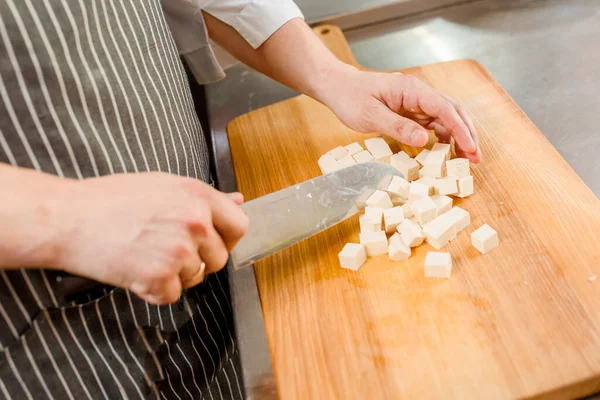 Cut white soft tofu cheese for ramen soup on kitchen . Chef cooks white soft cheese in restaurant. Dice cheese