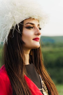 Georgian girl in papakha and red national dress with cross symbols. Attractive woman on the lake. Georgian culture lifestyle. Woman looks right side clipart