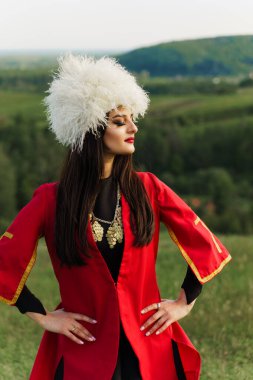 Georgian girl in papakha and red national dress with cross symbols. Attractive woman on the lake. Georgian culture lifestyle. Woman looks right side clipart