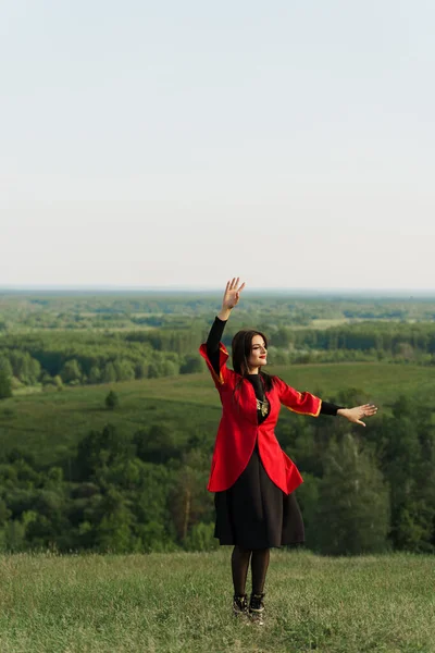 Georgian woman dances national dance in red national dress on the green hills of Georgia background. Georgian culture lifestyle.