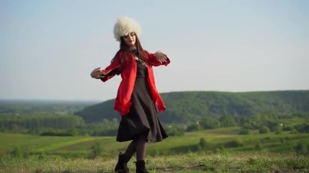 Gruzínská dívka v bílém papakha a červené národní šaty tance národní tanec s názvem: rachuli, acharuli, osuri, shalaxo, mtiuluri. na zelených kopcích gruzínského pozadí. Gruzínská kultura životního stylu.