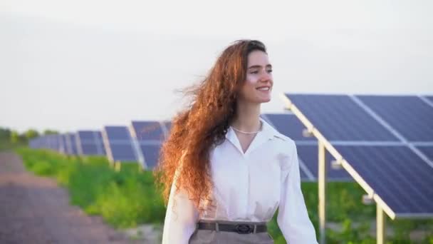 迷人的女孩在日落时走在地上的太阳能电池板旁边 女投资者穿着正式的白衬衫 免费家用电器 地球的可持续性 绿色能源 — 图库视频影像