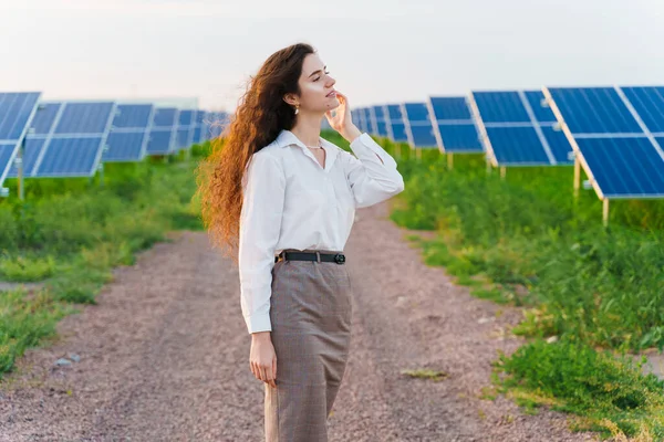 Girl stand and look left side between 2 Solar panels row on the ground at sunset. Free electricity for home. Sustainability of planet. Green energy. Solar cells power plant business.