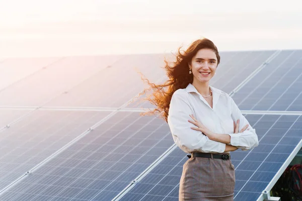 Güneş panelleri olan model gün batımında yerde duruyor. Beyaz tişörtlü kız elektrik santralinde gülümsüyor. Ev için bedava elektrik. Yeşil enerji. Güneş pilleri enerji santrali işi.
