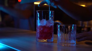 Barmen kırmızı vermut ve campari 'yi mavi ışıkta karıştırır. Barthender barda Americano kokteyli yapıyor.