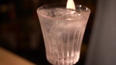 Barmen Fransız 75 'lik alkollü kokteyli ışıltılarla karıştırıyor ve bir parça buzu cama koyuyor. Barmen barda kuyruk kuyruğu yapıyor. Bar, restoran, bar, gece kulübü için adres