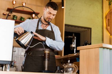 Yakışıklı barmen kafeteryada kahveyle birlikte uçağa sıcak su dolduruyor. Sakallı barista işe yarıyor. Kahveci tarafından kafede yapılan alternatif bir şey. İskandinav kahvesi demleme yöntemi.