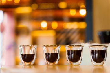 Arkaplanı bulanık, çift cam bardakta, 4 aromalı kahveli espresso. Çatı katındaki ahşap masada kahve fotografı.
