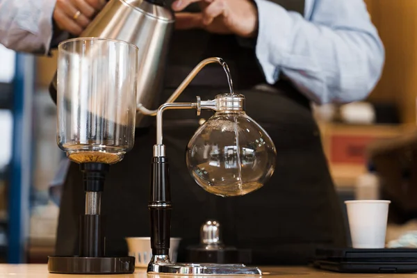 Syphon alternative method of making coffee. Barista pours hot boiling water in syphon device for coffee brewing in cafe. Scandinavian method of coffee making.