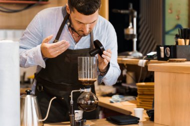 Barista sifon cihazındaki kahveyi kokluyor. Barista sifondaki kahveyi kontrol ediyor. Kahve demleme alternatif sifon metodu. Kafe ve restoran için sosyal ağlara yönlendir.