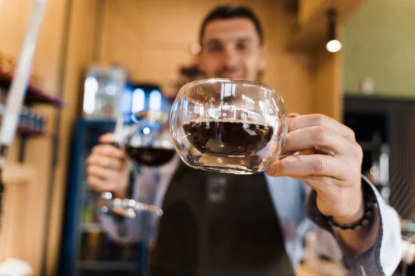 Double glass cup with coffee in cafe. Barista gives a cup of coffee to you. Alternative coffee brewing using Syphon device.