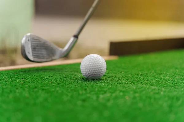 Close-up playing in mini-golf on the green grass using niblick. Player hits white ball. Golf sport game. Advert for golf club
