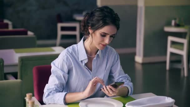 Ділова жінка в офіційній сорочці, розмовляє онлайн зі своїми колегами, використовуючи смартфон у сучасному ресторані в люксовому часі. Соціальне дистанціювання . — стокове відео