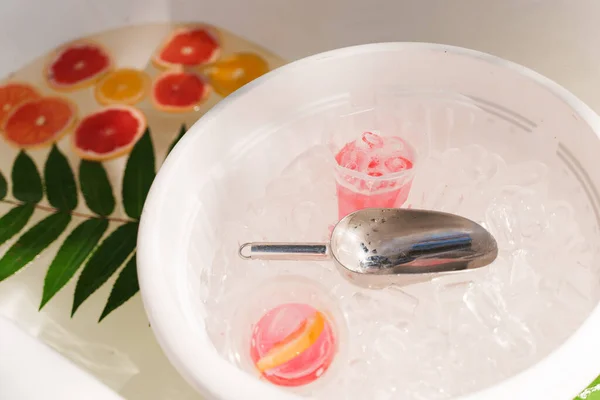 Large bathroom with ice cubes, fruits grapefruit, orange, lemon, green leaves and cocktails. Welcome zone of drinks with colourful lemonades. Non-alcoholic healthy drinks.