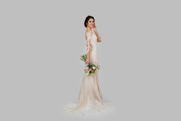 Young attractive bride with bouquet in modern bridal look with cap sleeves and an illusion neckline top off the column silhouette and sweeping train. Bride girl in studio on white background