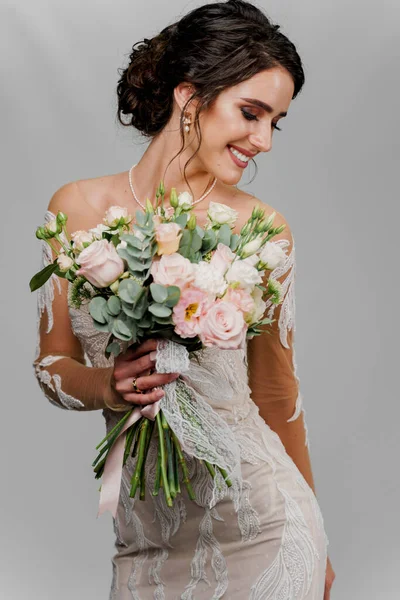 Bride with wedding bouquet looks right side and smiles. Attractive girl vertical portrait for social networks. Girl in wedding gown on blank background