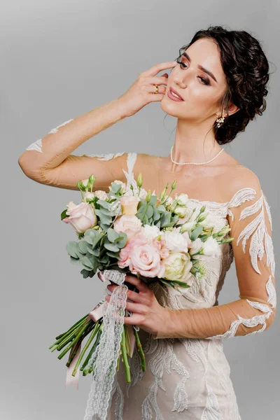 Attractive girl bride with wedding bouquet smiles, looks left side and touches her face. Attractive girl vertical portrait for social networks. Girl in wedding gown on blank background