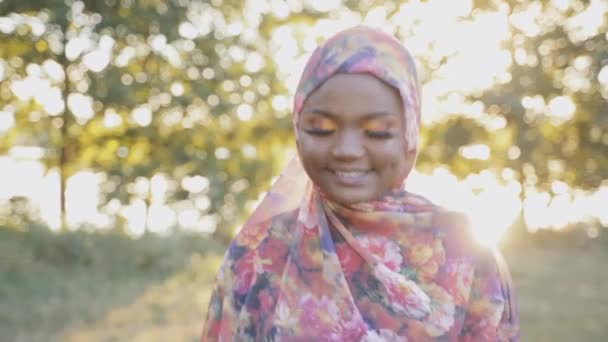 Muzułmanka pochodzenia afrykańskiego, nosząca tradycyjny kolorowy hidżab na zielonym tle ze światłem słonecznym. Arabski islam ubrania religijne. Ładna czarna dziewczyna uśmiecha się — Wideo stockowe