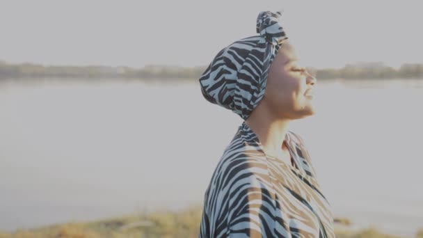 Muslimische Frau afrikanischer Herkunft trägt traditionellen bunten Hijab geht in der Nähe des Sees und lächelt. Arabische islamische Religionskleidung. Hübsches schwarzes Mädchen lächelt — Stockvideo