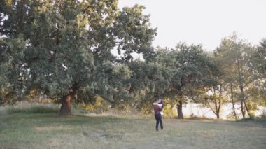 Karışık çiftlerin yeşil arka planda dönen ve kucaklaşan büyük ağacın yanında mutlu Müslüman aşk hikayesi. Başörtülü kadın erkeğine bakıyor. Online randevu ajansına yönlendir