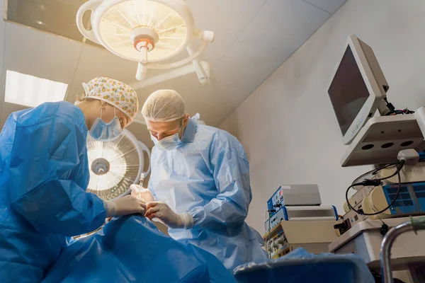Tıbbi klinikte yüz bölgesinin değiştirilmesi için Blepharoplasty estetik ameliyatı. İki doktor kadınlar için estetik ameliyat yapıyor. Cerrah göz kapağına dikiş atar.