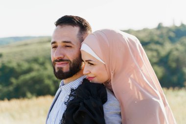 Müslüman aşk hikayesi yakın plan. Yeşil tepelerde karışık gülücükler ve kucaklaşmalar. Başörtülü kadın erkeğine bakıyor. Online randevu ajansına yönlendir
