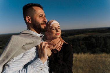 Mavi gökyüzü arka planında Müslümanların aşk hikayesi. Neşeli karışık gülüşler ve kucaklaşmalar. Başörtülü kadın erkeğine bakıyor. Online randevu ajansına yönlendir