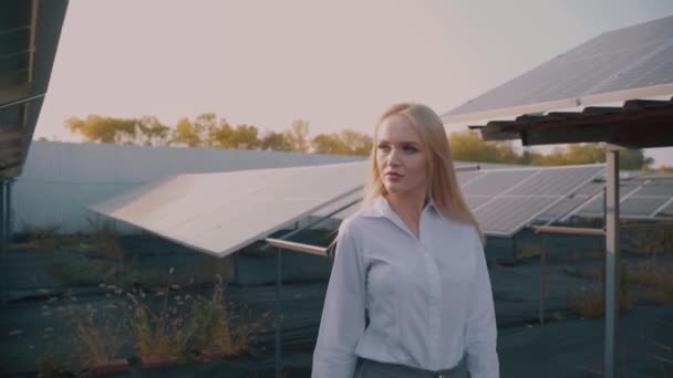 Frau geht in der Nähe von Sonnenkollektoren, die bei Sonnenuntergang auf dem Boden liegen und Solarzellen betrachten. Investorin trägt formell weißes Hemd. Kostenloser Strom für zu Hause. Nachhaltigkeit des Planeten. Grüne Energie. — Stockvideo