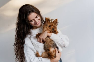 Köpek Yorkshire Terrier gülüşlü çekici bir kadın. Fotoğrafı kapat. Hayvan bakımı. İnsanlar ve evcil hayvanlar. Kız kahverengi köpeği beyaz arka planda tutuyor