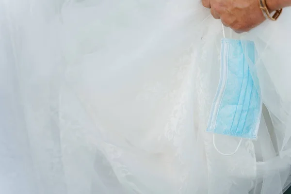 Medical mask and wedding dress close up. Blue surgical mask on the white background