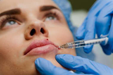 Çekici bir kız için yakın plan dudak büyütme iğneleri. Estetik cerrah tıbbi klinikte dudağına iğne yapar. Kozmetik yenileme yüz tedavisi. Reklam için boş alan