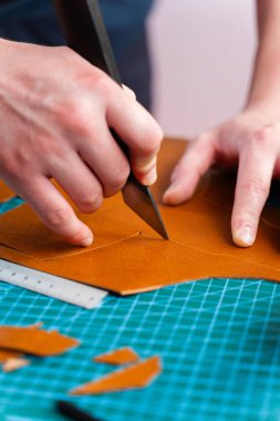 Bıçak ve cetvelle deri keser. Zanaatkar el yapımı mallar için hakiki deri parçalarını şekillendirmek için bir bıçak ve cetvel kullanır. Zanaatkarlar kenarlarını düzeltir ve hakiki deri hazırlarlar.