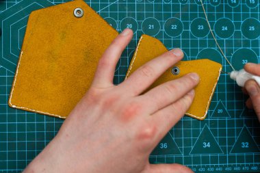 Deri kenarlara yapıştırıcı sürüyorum. Deri ürünler üretimi güçlü bir yapıştırıcıyı güvenli bir şekilde kenetleyerek başlar. Deri ustaları dikiş atmadan önce kenar hazırlamak için yapıştırıcı kullanır.