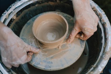 Potter şekilli kil kaseyi tekerlekten ayırmak için tel kullanıyor. Seramik çalışmalar, tekerlekteki kilin kesin kesimini gösteriyor. Tekerlekteki kil çömleği kabloyla kesiyor.