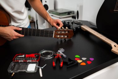 Gitar akort süreci raptiyeleri ayarlamayı ve daha iyi ses için yeni teller hazırlamayı içeriyor. Gitar teli değiştirme ve akort hazırlığı. Müzisyen bir gitarı araçlar ve yedek teller kullanarak ezer
