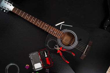Gitar teli yerine aletler. Yeni teller ve masada gerekli aletlerle akustik gitar kurulumu devam ediyor. Akustik gitar yanında pense ve tornavida takımı ile yeniden dizme işlemi