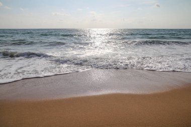 Kumlu sahilde okyanus dalgası ve kumlu zeminde ayak izleri.