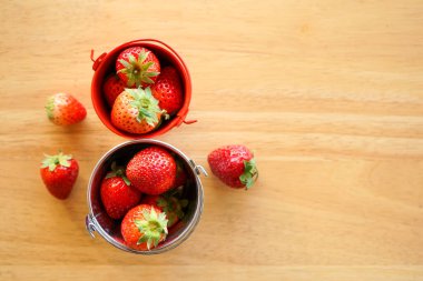 Tahta masadaki küçük paslanmaz çelik kovalarla taze çileklerin üst görüntüsü.  
